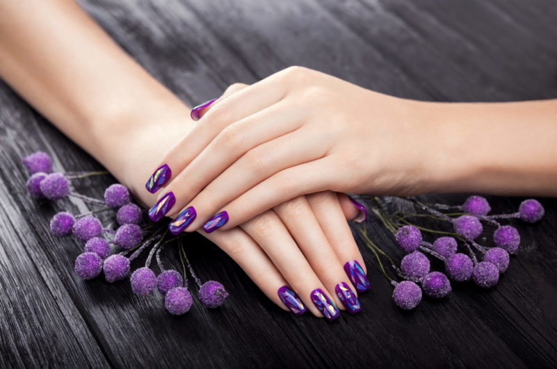 Dos manos con manicura violeta sobre una tabla de madera negra