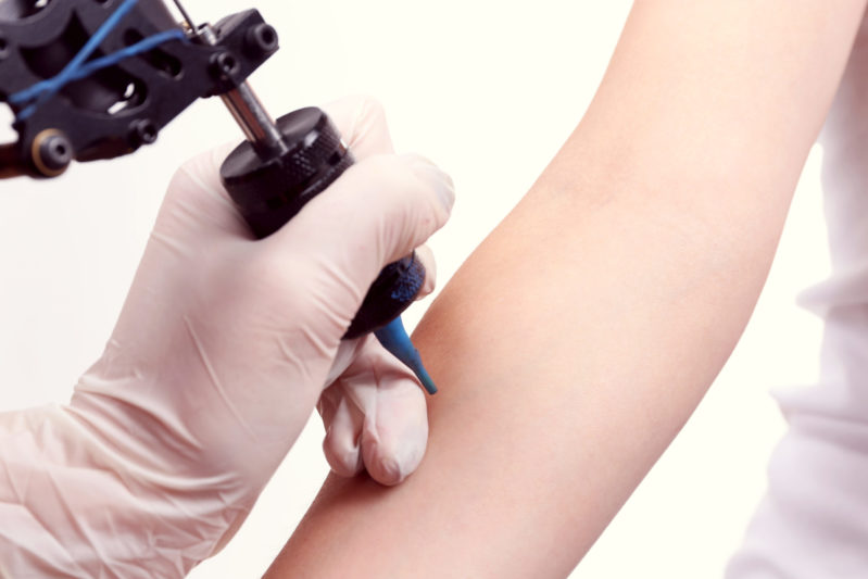 Tatuador tatua sobre el brazo de la mujer con fondo blanco
