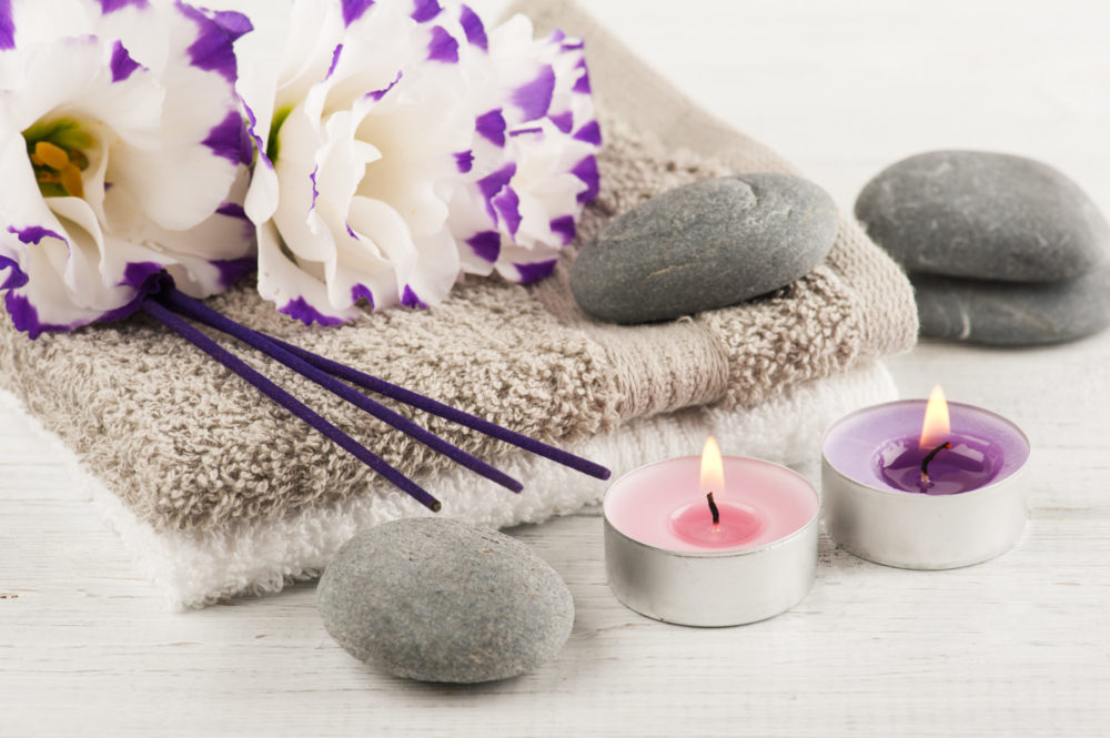 Dos toallas con velas moradas encendidas y unas flores de lavanda con unas piedras grises alrededor